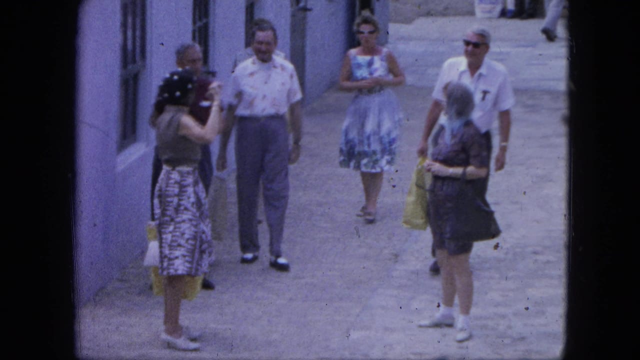 A 1964 Nassau alley scene shows a woman holding a camera near tourists in patterned summer clothing and sunglasses.