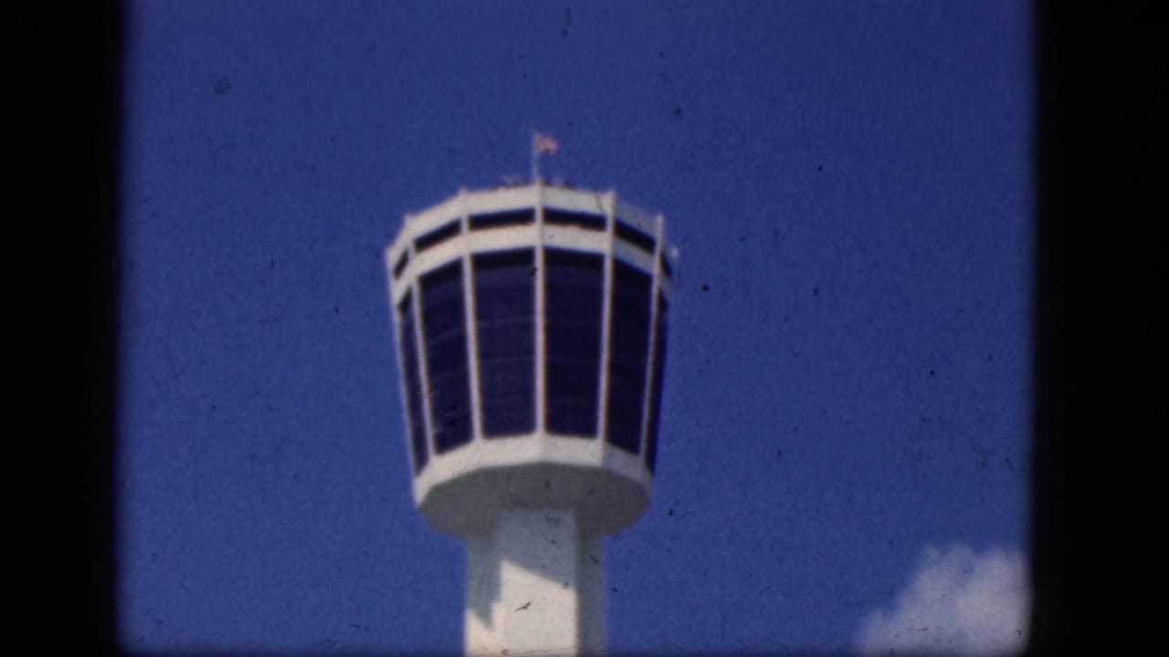 Upper section of a white airport control tower against blue sky.
