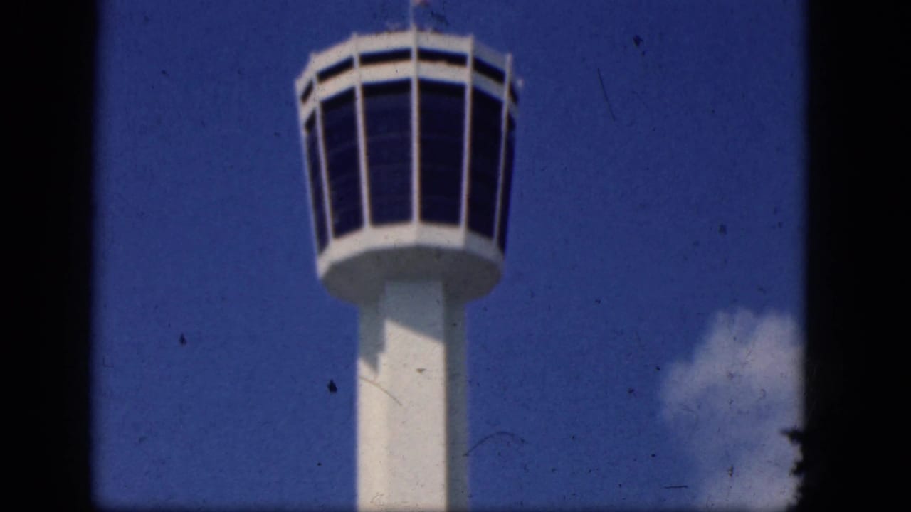 Airport control tower top and column seen from below with clouds nearby.