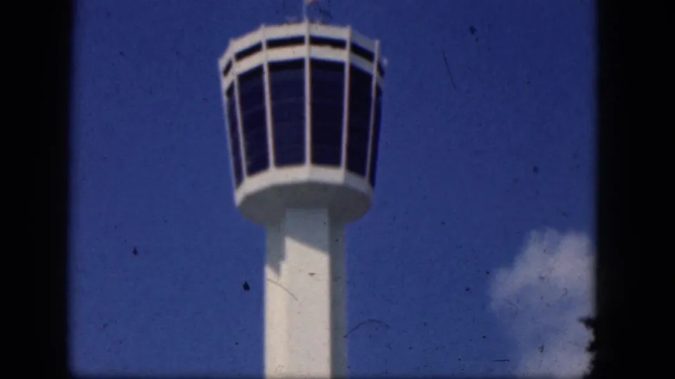White control tower with dark windows and a tall column, filmed upward against blue sky in the supplied Niagra Falls, Canada setting.