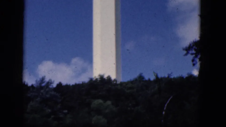 The 8mm view holds on the tower shaft above dense trees, with saturated sky color and visible film dust from the scan.