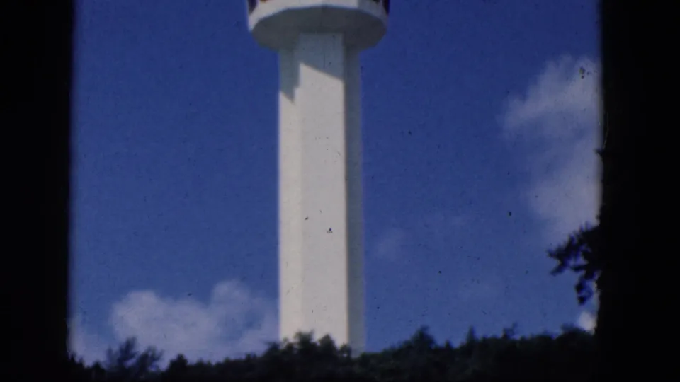 The tower top and white shaft are visible above trees in a Niagara Falls, Canada home-movie frame from 1964.