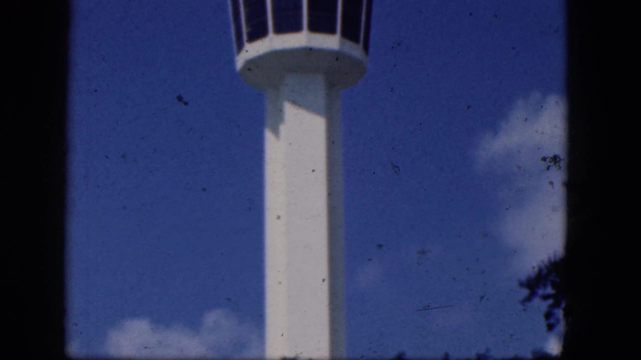 White airport control tower partly cropped against blue sky and small clouds.