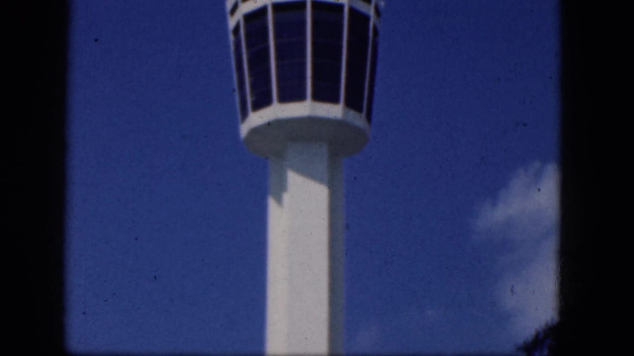 Upper portion of a white control tower with dark windows against blue sky.