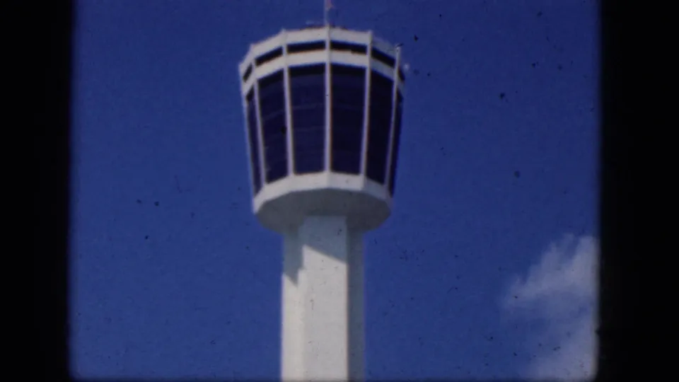 The tower's circular observation cab is centered over its white shaft, with blue sky, light cloud, and visible 8mm film grain.