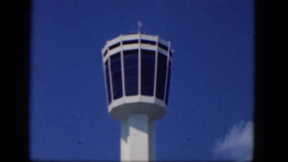 A small flag is visible atop the windowed airport control tower cab, filmed against blue sky in the Niagara Falls, Canada 1964 reel.