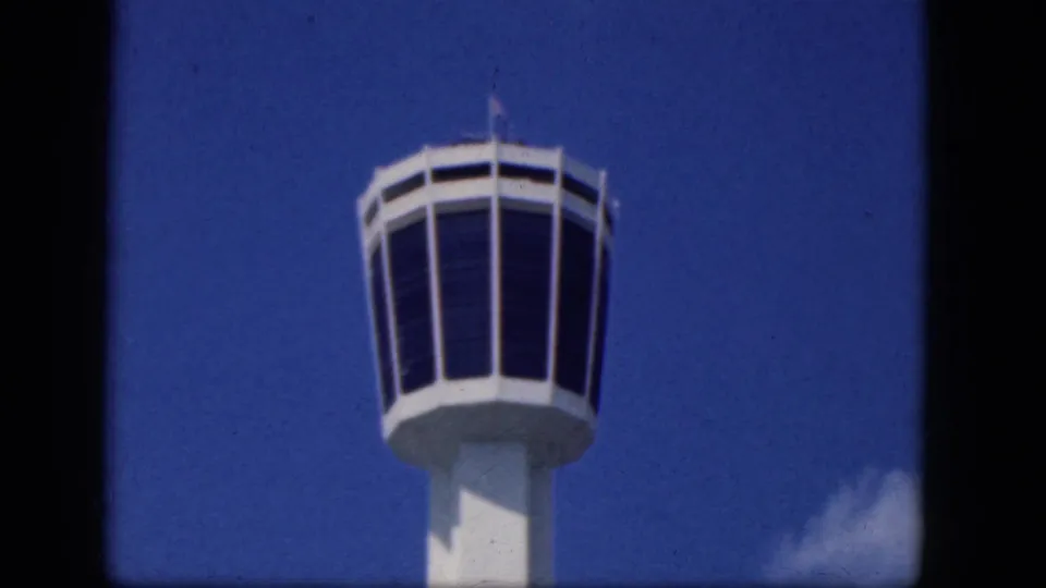 1964 Niagara Falls Canada home-movie frame showing a white airport control tower with dark windows against blue sky.