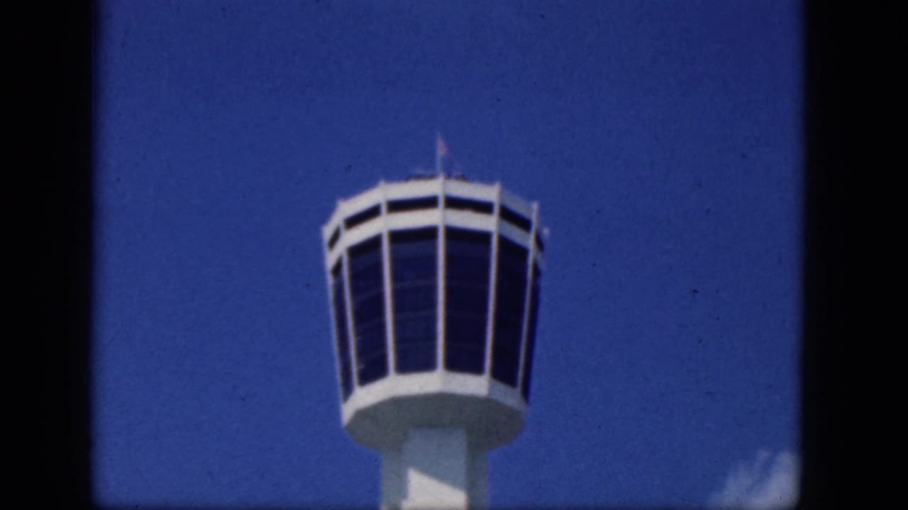 Control tower top framed against blue sky with a small cloud near the lower right.
