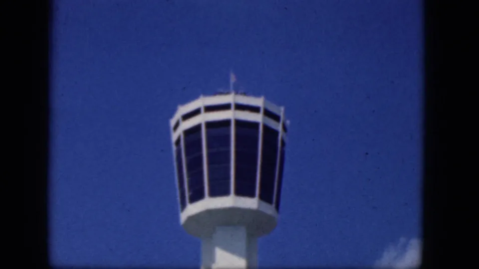 1964 Niagara Falls Canada frame of a white airport control tower crown, dark glass panels, and blue sky with a small cloud.