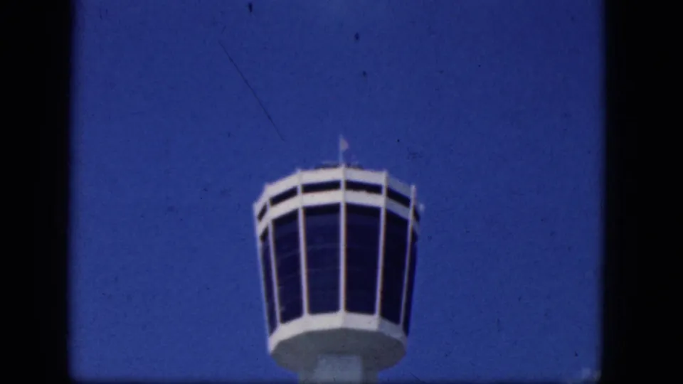 1964 Niagara Falls Canada home-movie still with the airport control tower lower in frame beneath open blue sky.