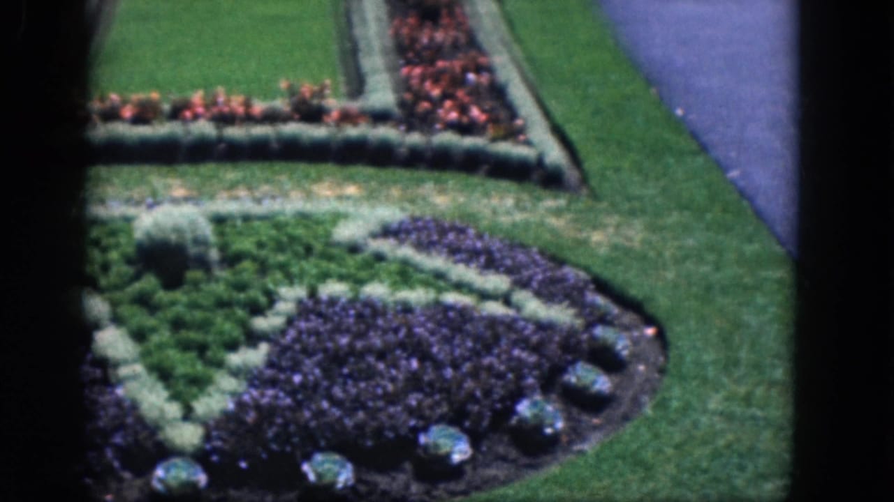 Formal flowerbeds with purple blooms, hedges, lawn, and paved paths.