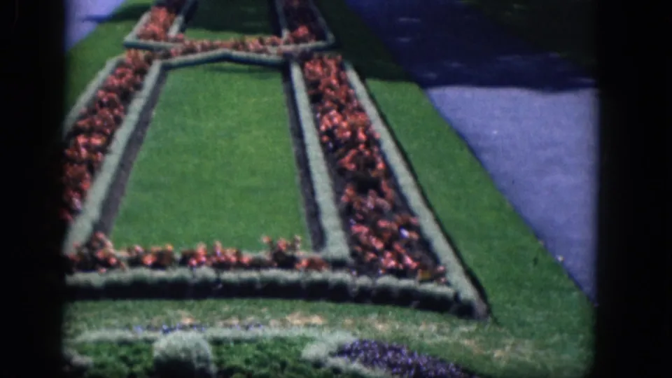 1964 8mm view of Niagara Falls, Canada garden landscaping with red flowers, clipped hedges, green lawn, and a paved path.