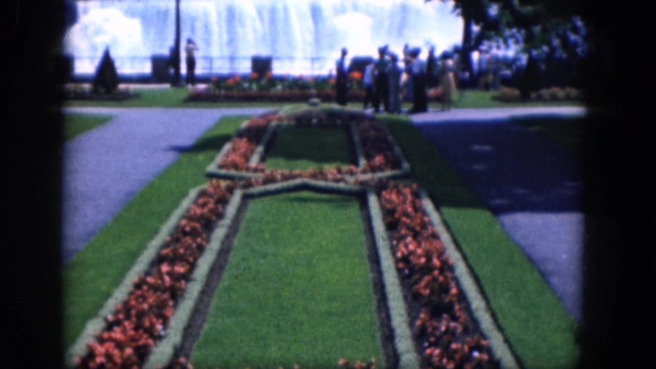 Symmetrical garden beds run toward a misty waterfall with people standing near the railing.
