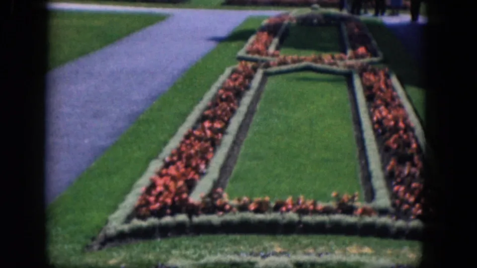 1964 Niagara Falls, Canada frame with a closer pan view of red flower beds, clipped borders, lawn, and paved walkway.