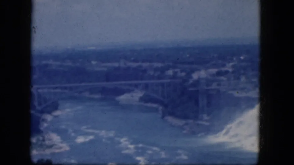 Elevated 8mm frame from Niagara Falls, Canada, showing the river, bridge and partial waterfall under a hazy sky.