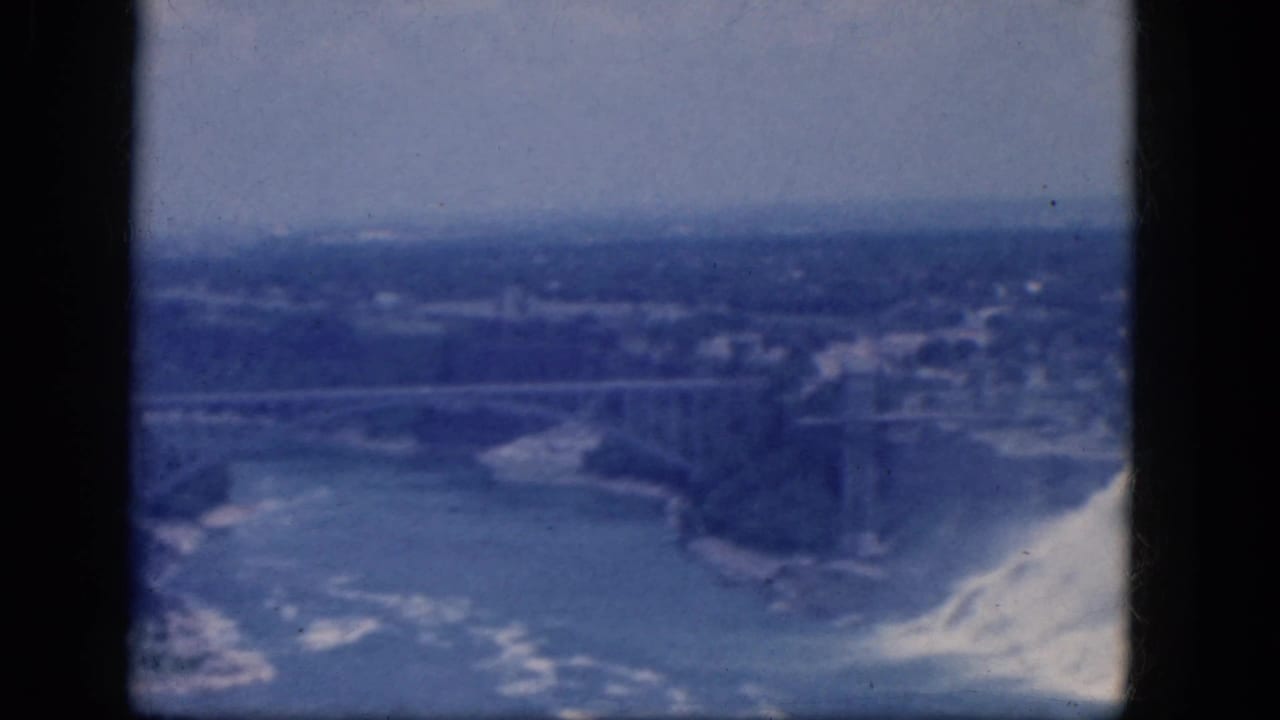 Elevated view of Niagara Falls with a bridge across the gorge and water mist at right.