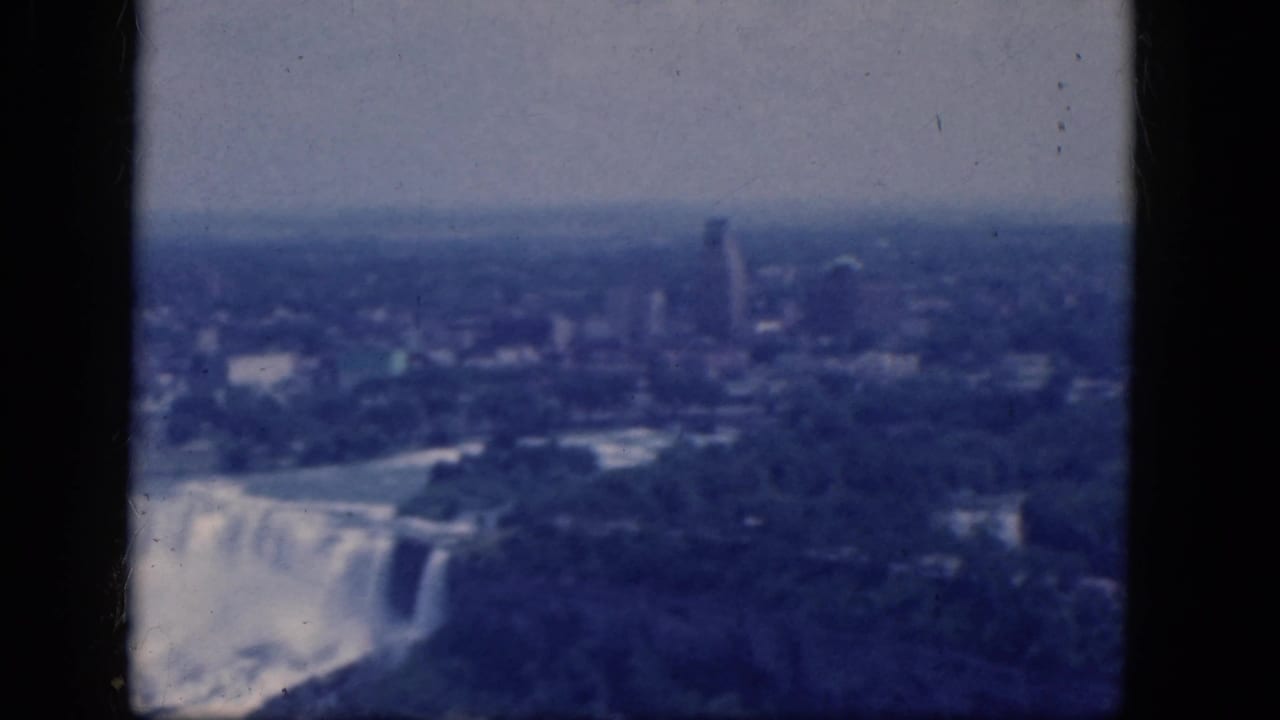 Niagara Falls seen from above with mist, trees, skyline, and dark film borders.