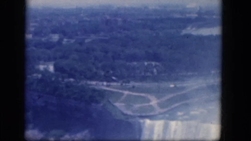 1964 8mm aerial view of Horseshoe Falls at Niagara Falls, Canada, showing the brink, mist, shoreline, and park paths.