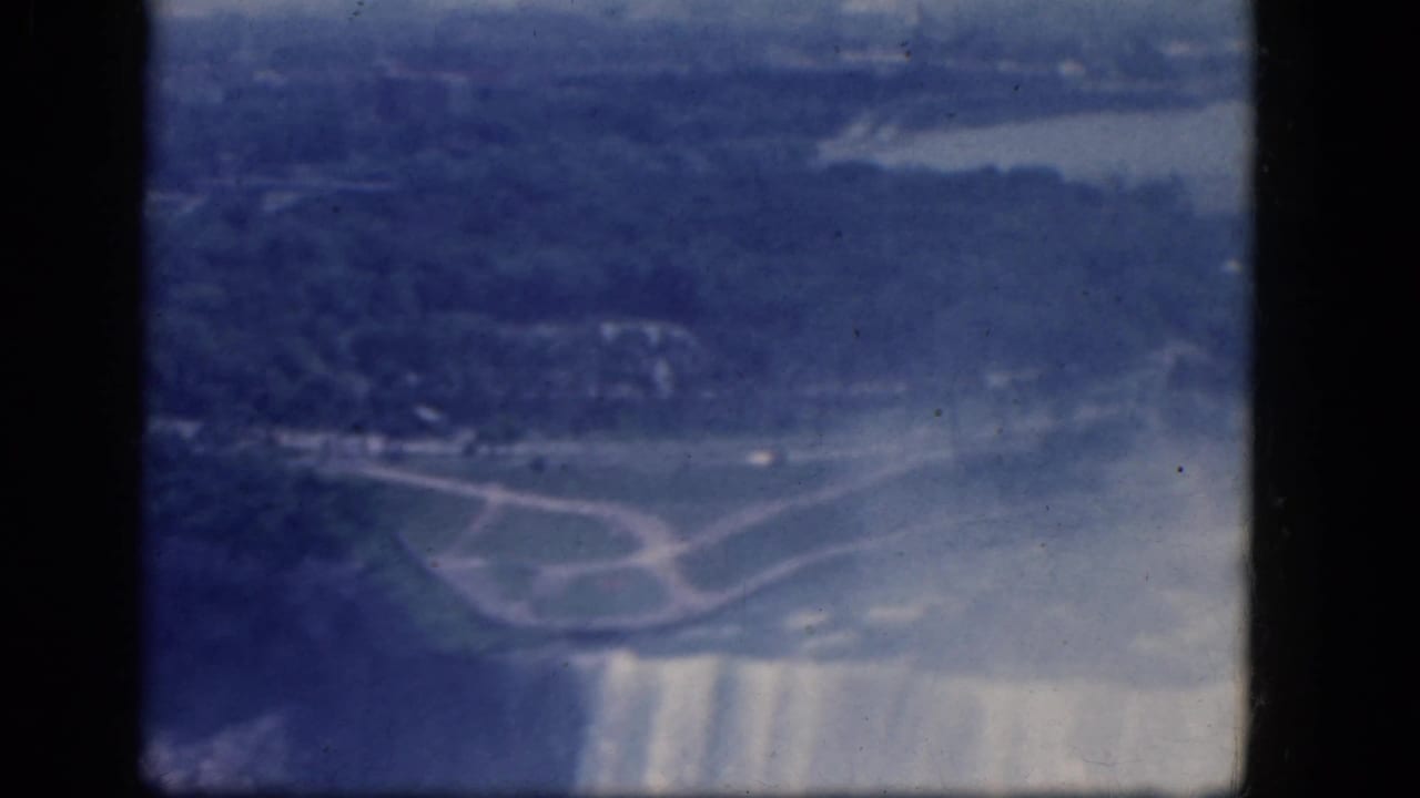Aerial view across the falls brink, mist plume, shoreline, and curved paths.