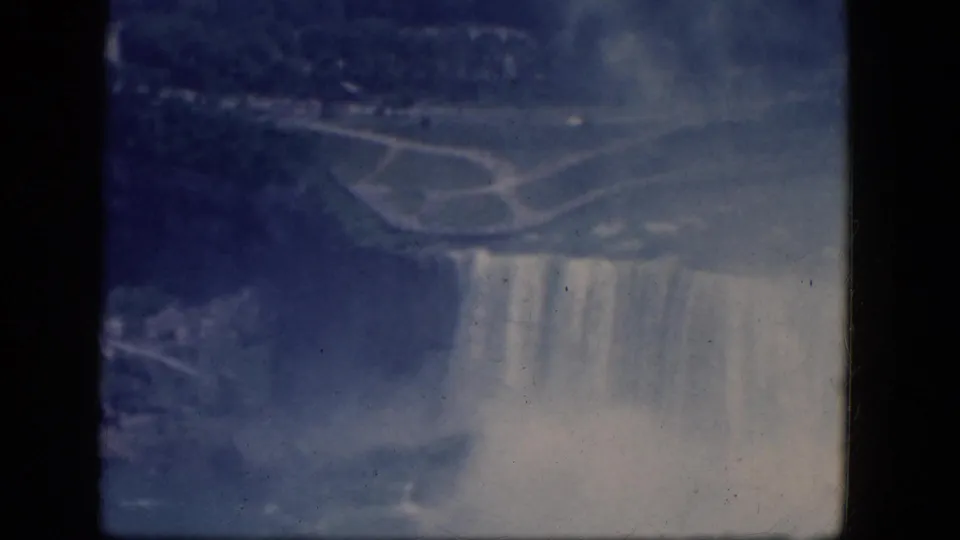 1964 8mm view of the Canadian side of Niagara Falls, with cascading water, mist, and parkland seen from above.