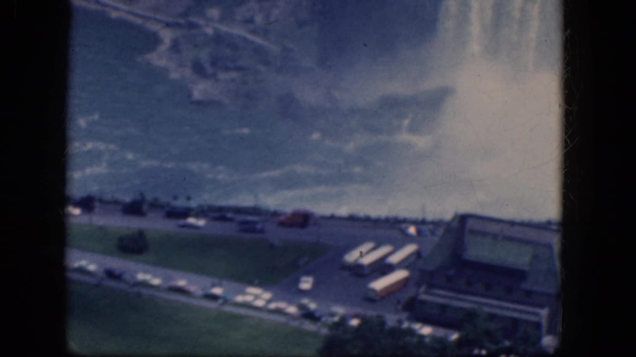 Aerial view of waterfall mist, roads, parked cars, buses, lawns, and a low building.
