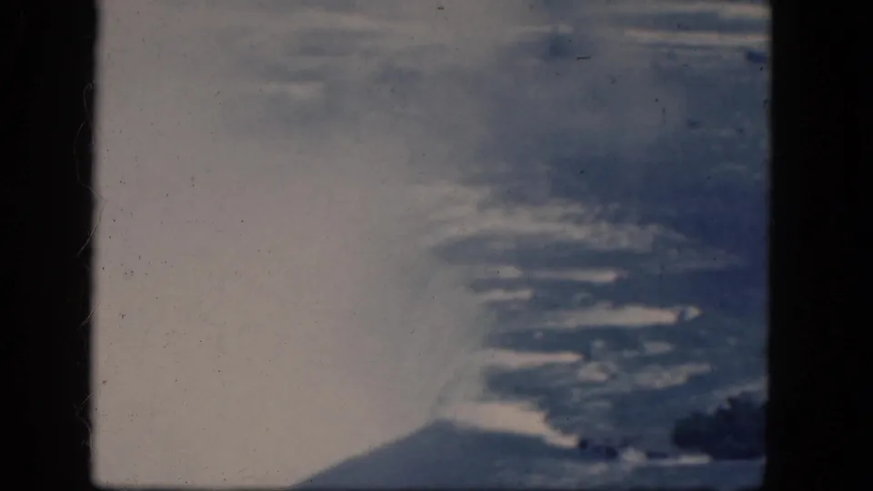 1964 Niagara Falls aerial frame with bright mist, textured water, a dark lower-edge shoreline area, and visible 8mm frame borders.