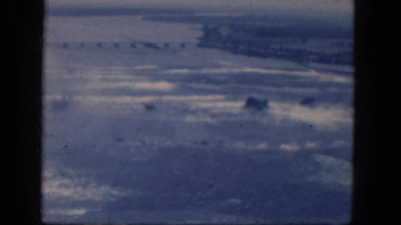 Hazy elevated view over water and distant shoreline framed by dark film-gate edges.