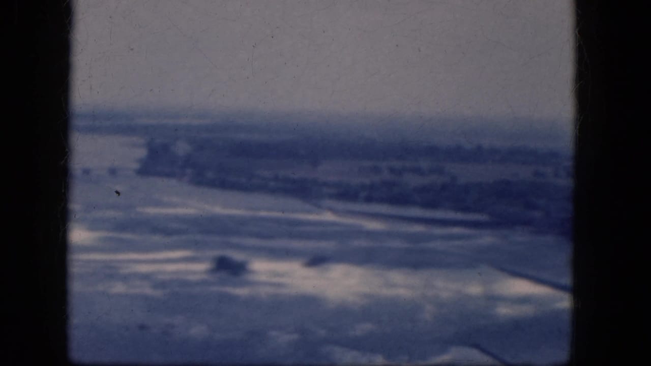 Distant aerial terrain with waterlike shapes and a dark vertical frame edge.