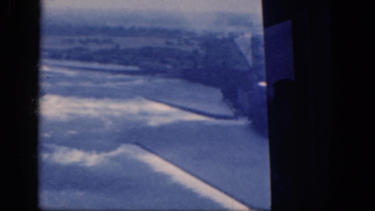 Dark airplane window bars over a blue-white aerial landscape below.