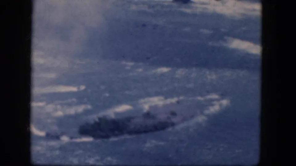 A cool-toned 1964 8mm aerial view shows a dark window frame beside blue-white ground textures and a darker land or ice patch.