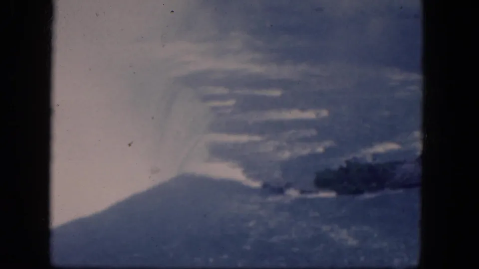 1964 home-movie frame showing Niagara Falls mist and water from above, with the rocky island partly cropped by the frame.