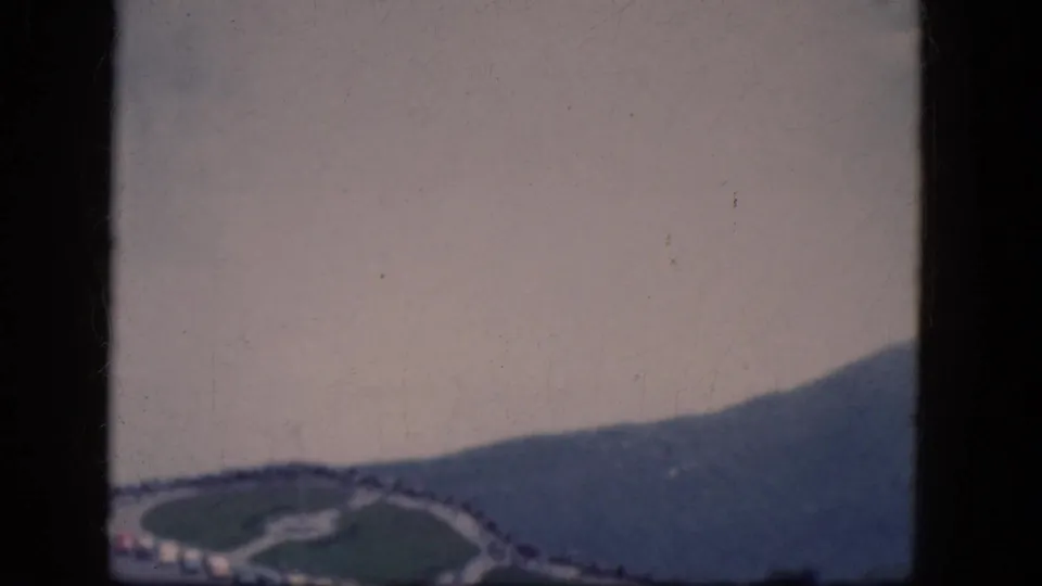 1964 8mm high-angle view near Niagara Falls, Canada, with water, a curving road, green areas, and parked cars.