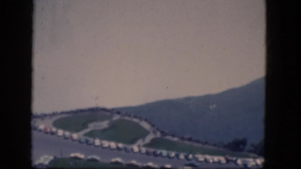 Faded 1964 8mm frame near Niagara Falls, Canada, showing a road, parking rows, water, and a dark hillside.