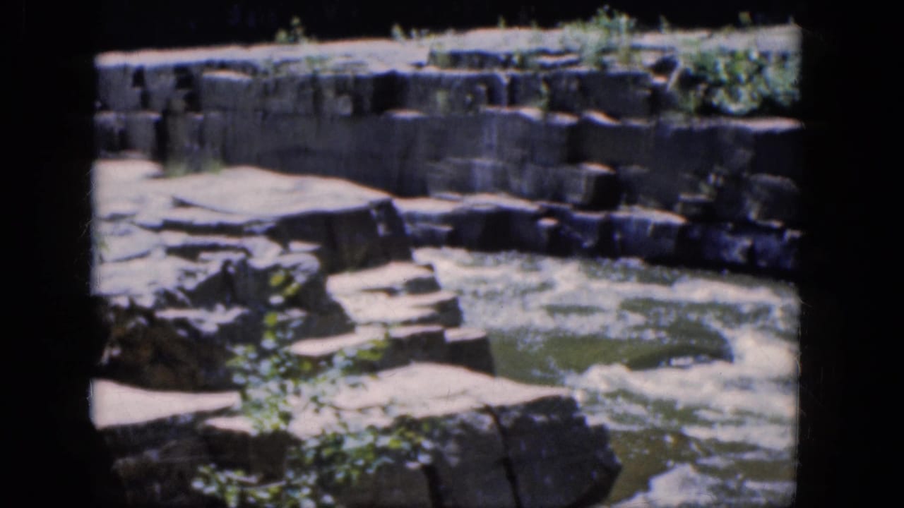 Foaming water beside flat stone ledges and blocky rock walls.