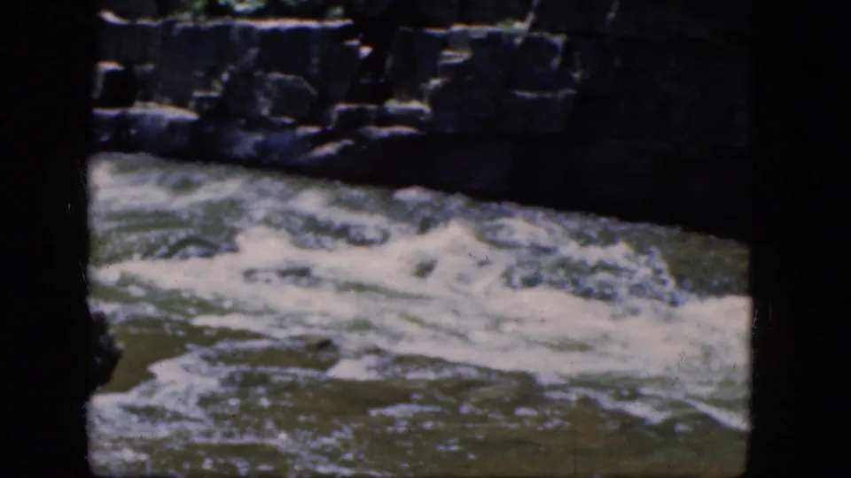 Vintage 8mm view of churning Niagara Falls river water with dark rock formations and soft home-movie color.