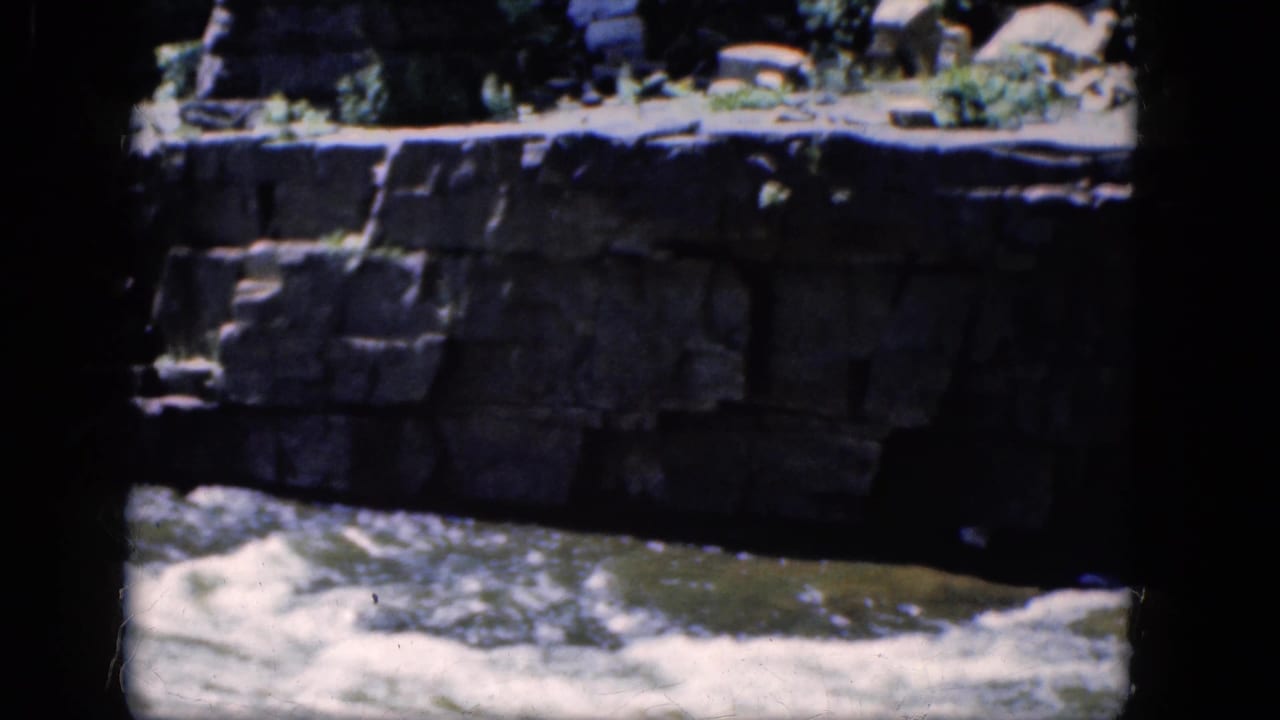 White water flows along a stone wall, partly obscured by dark frame borders.
