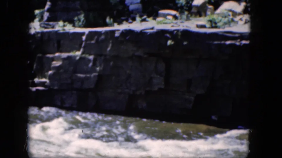 A Niagara Falls home-movie frame shows turbulent water moving past stonework, with heavy dark borders from the 8mm scan.