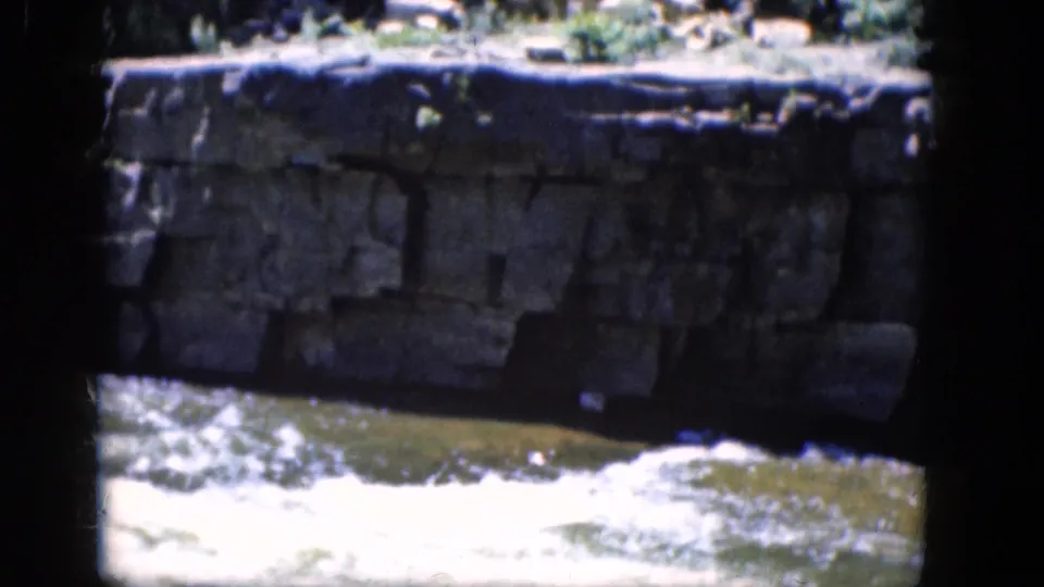 The frame shows foaming water below a weathered stone embankment in 1964 Niagara Falls travel footage.
