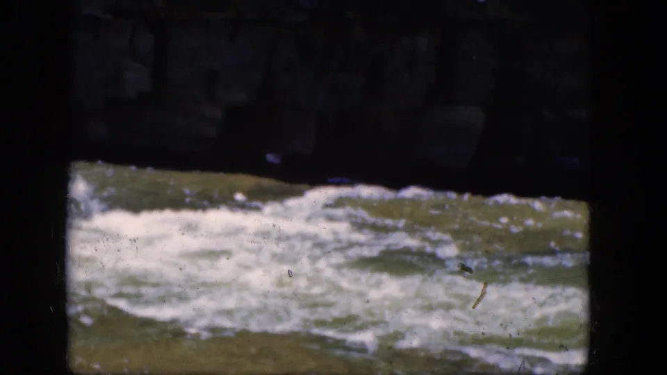 An 8mm Niagara Falls frame shows churning water below shadowed stonework, with visible grain, dust, and dark scan borders.