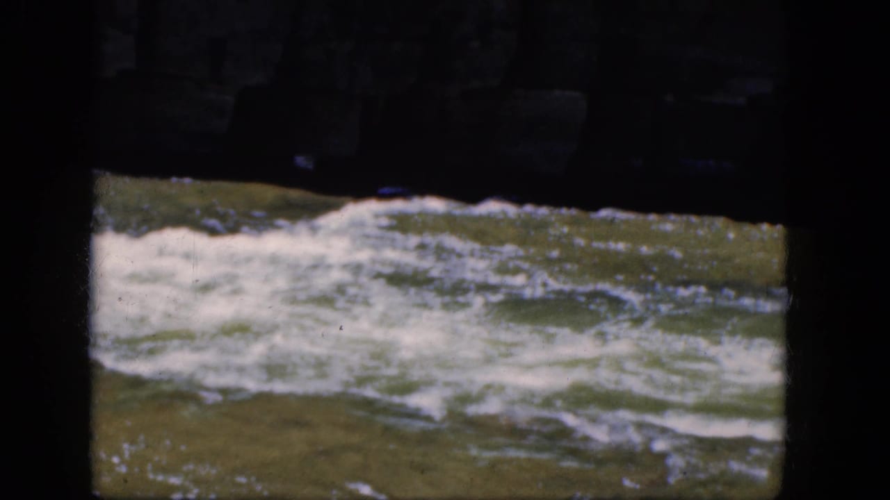 Foaming greenish river water seen through a dark stone opening.