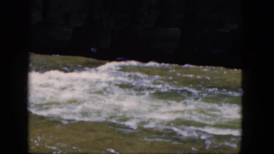 1964 8mm Niagara Falls-area footage showing fast river current framed by a shadowed stone bridge or underpass.