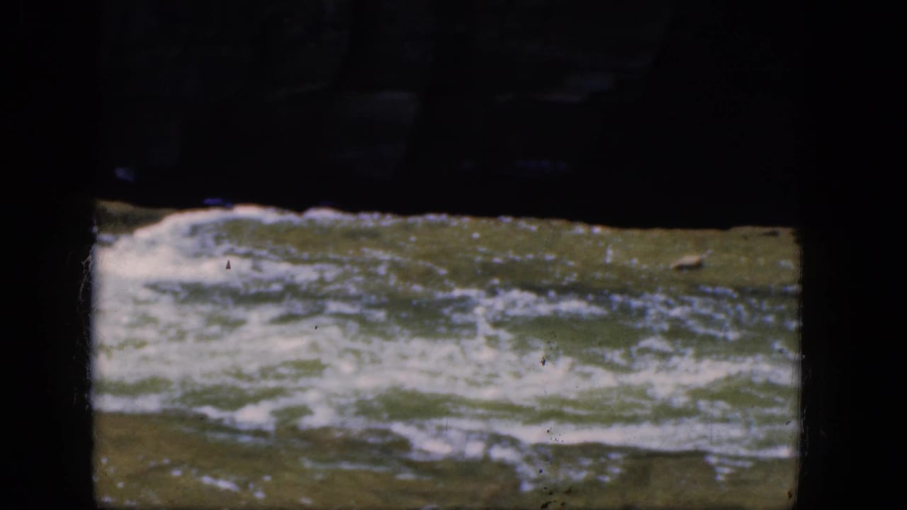 Rushing river current with white foam under a dark overhead structure.