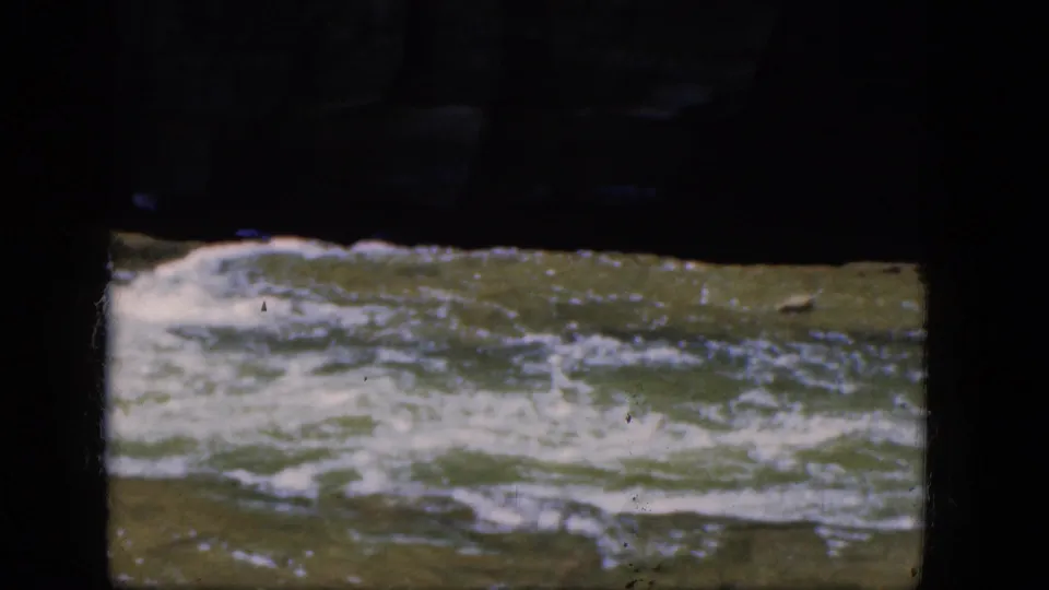 Fast, foaming river water passes beneath a shadowed structure in 1964 Niagara Falls-area home-movie footage.
