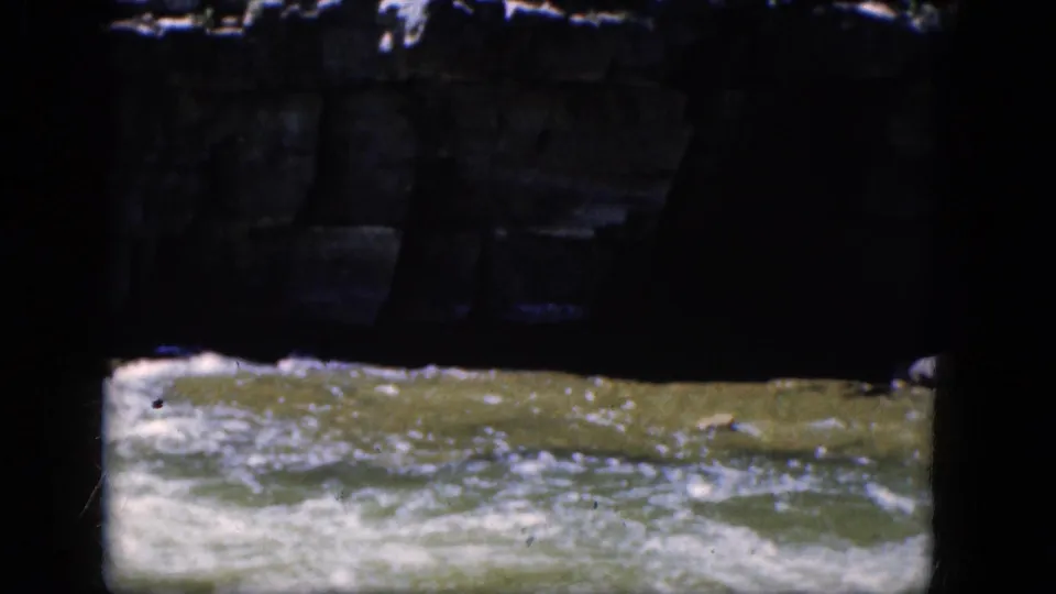 A low, shadow-framed view catches turbulent river water and foam in 1964 Niagara Falls-area 8mm footage.
