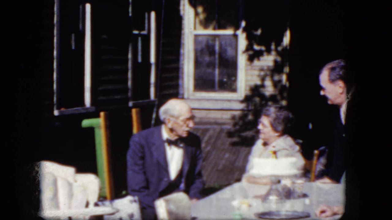 Older couple and younger man seated at an outdoor table on a porch.