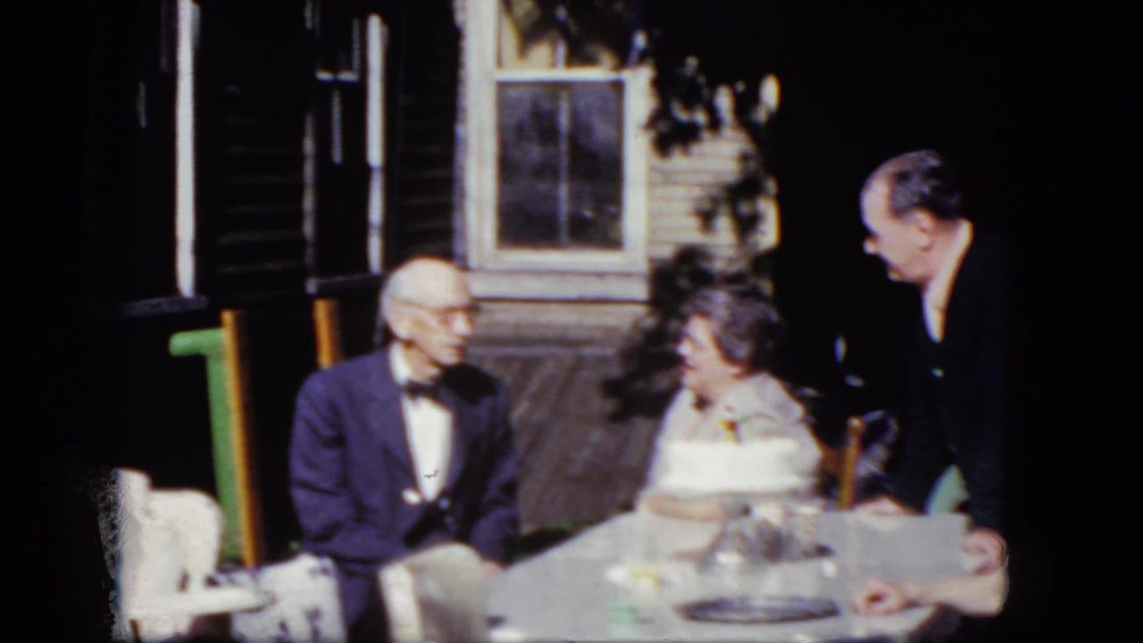 Older man and woman seated at a table as a younger man leans nearby.