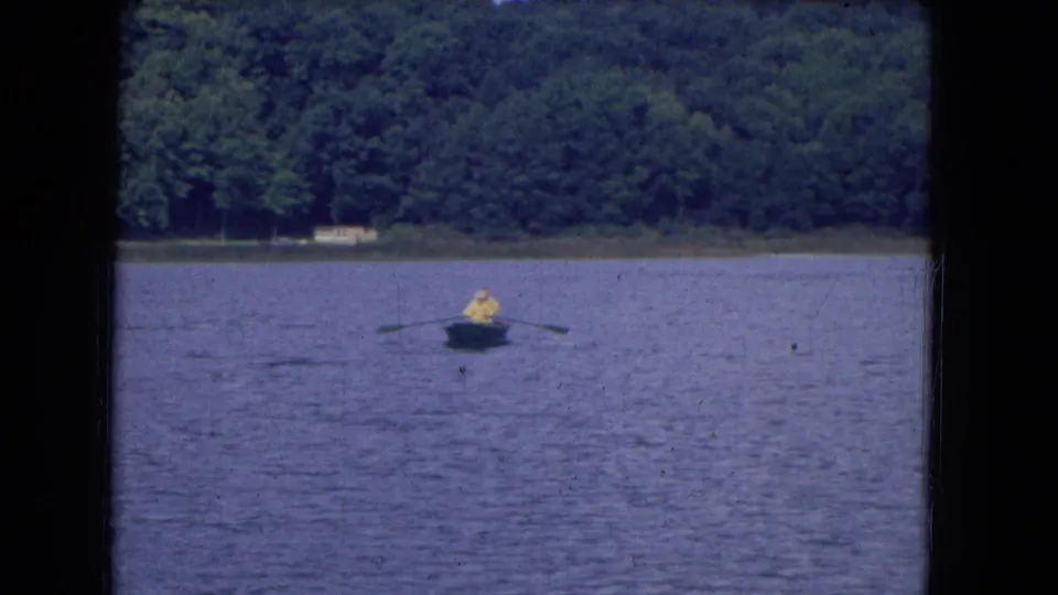 Distant rowboat on a lake near Niagara Falls, New York, with one visible person and dense green trees beyond the water.
