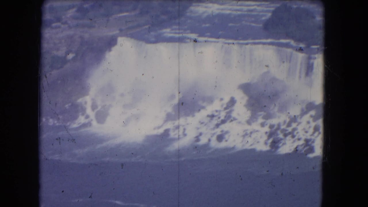 Elevated view of Niagara Falls with a broad waterfall curtain and mist below.
