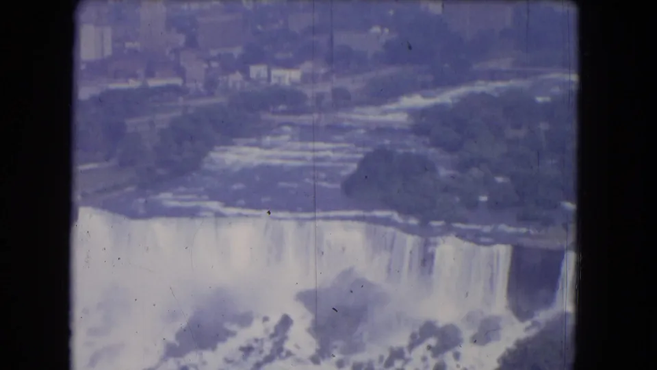 1964 8mm home-movie view of Niagara Falls including shoreline, distant structures, waterfall edge, and mist.