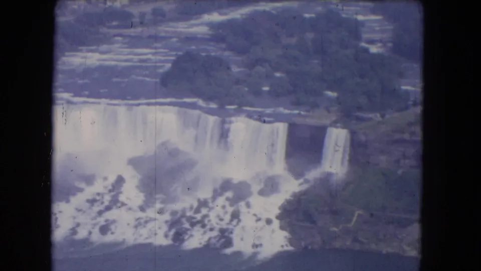1964 8mm aerial view of Niagara Falls with cascading water, mist, rocks, and dark film-frame borders.